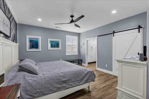 Bedroom with a barn door, hardwood / wood-style floors, ceiling fan, and recessed lighting