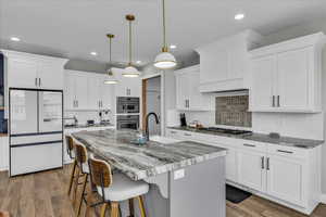 Kitchen featuring stainless steel appliances, a breakfast bar area, white cabinets, and decorative light fixtures