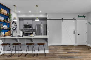 Kitchen featuring a barn door, stainless steel appliances, light wood finished floors, gray cabinetry, and a breakfast bar
