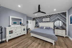 Bedroom featuring an accent wall, wallpapered walls, dark wood finished floors, a ceiling fan, and recessed lighting