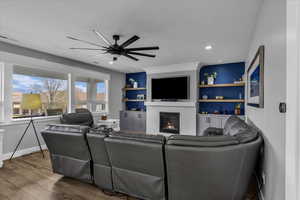 Living room with wood finished floors, ceiling fan, a brick fireplace, built in shelves, and recessed lighting