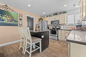 Kitchen with stainless steel appliances, a kitchen bar, tasteful backsplash, dark stone countertops, and a kitchen island