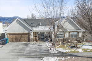 View of front of property with covered porch, a garage, driveway, stone siding, and roof with shingles