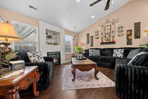 Living room featuring lofted ceiling, a ceiling fan, a large fireplace, wood finished floors, and built in features