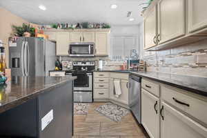 Kitchen with stainless steel appliances, dark stone counters, two tone color scheme, recessed lighting, and tasteful backsplash