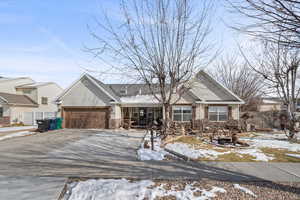 Single story home with covered porch, an attached garage, stone siding, and driveway
