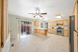 Kitchen featuring a peninsula, light countertops, stainless steel appliances, a ceiling fan, and light tile patterned floors
