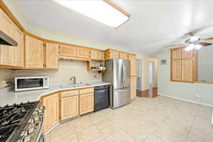 Kitchen with light wood finish cabinetry, light countertops, a ceiling fan, black dishwasher, and white microwave