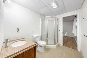 Full bath featuring vanity, a shower stall, a drop ceiling, and light tile patterned floors