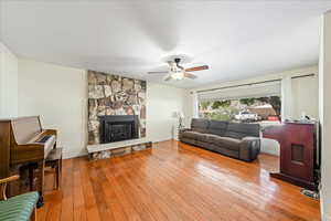 Living room with light wood-type flooring, a ceiling fan, and a stone fireplace