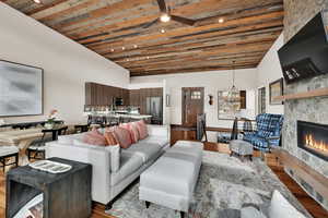 Living room with ceiling fan, a glass covered fireplace, wood finished floors, a chandelier, and a high wood ceiling