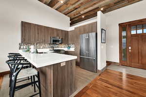 Kitchen featuring light wood-type flooring, stainless steel appliances, wood ceiling, a peninsula, and a kitchen breakfast bar