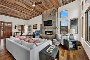 Living room featuring dark wood-style flooring, a stone fireplace, healthy amount of natural light, ceiling fan, and a high wooden ceiling