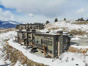 Snow covered back of property featuring stone siding, a mountain view, and a chimney