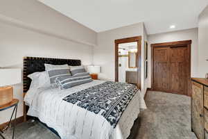 Carpeted bedroom featuring ensuite bath and baseboards