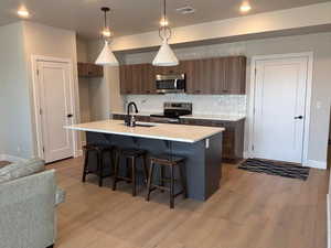 Kitchen with a breakfast bar area, stainless steel appliances, pendant lighting, a kitchen island with sink, and light wood-style floors