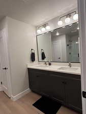 Full bathroom with double vanity, light wood-style flooring, a shower stall, and a textured ceiling