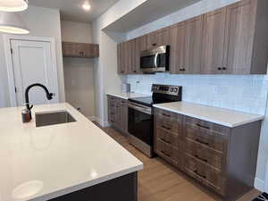 Kitchen featuring stainless steel appliances, light wood-style flooring, tasteful backsplash, light stone countertops, and wood finish cabinetry