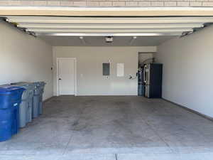 Garage with freestanding refrigerator, electric panel, and water heater