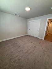 Unfurnished bedroom with dark carpet, a closet, and a textured ceiling
