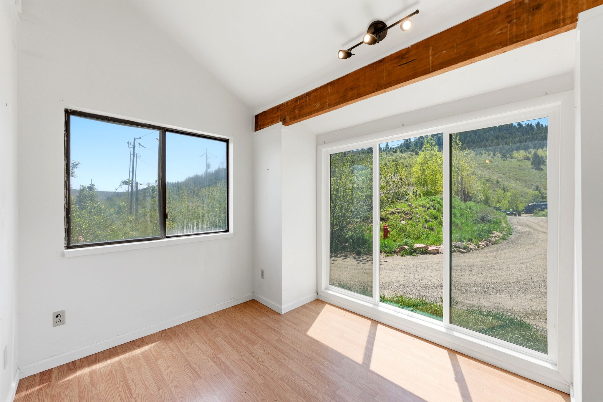 Vaulted ceiling featuring an exposed wood beam, recessed track lighting, wood-finish flooring, a large sliding glass door, and an additional window