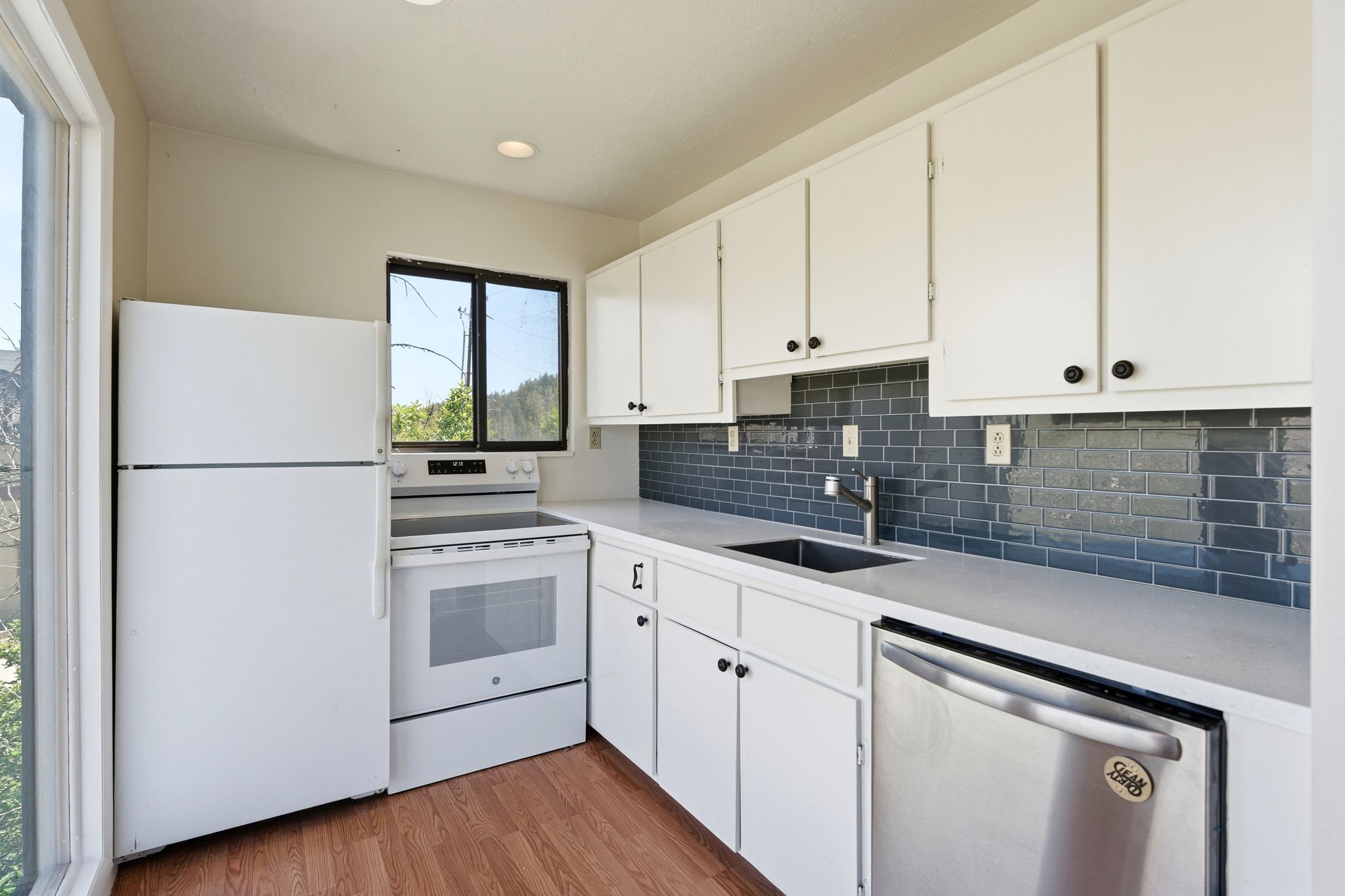 Bright kitchen featuring white cabinetry with dark hardware, a subway tile backsplash, light countertops, wood-finish flooring, and stainless steel appliances