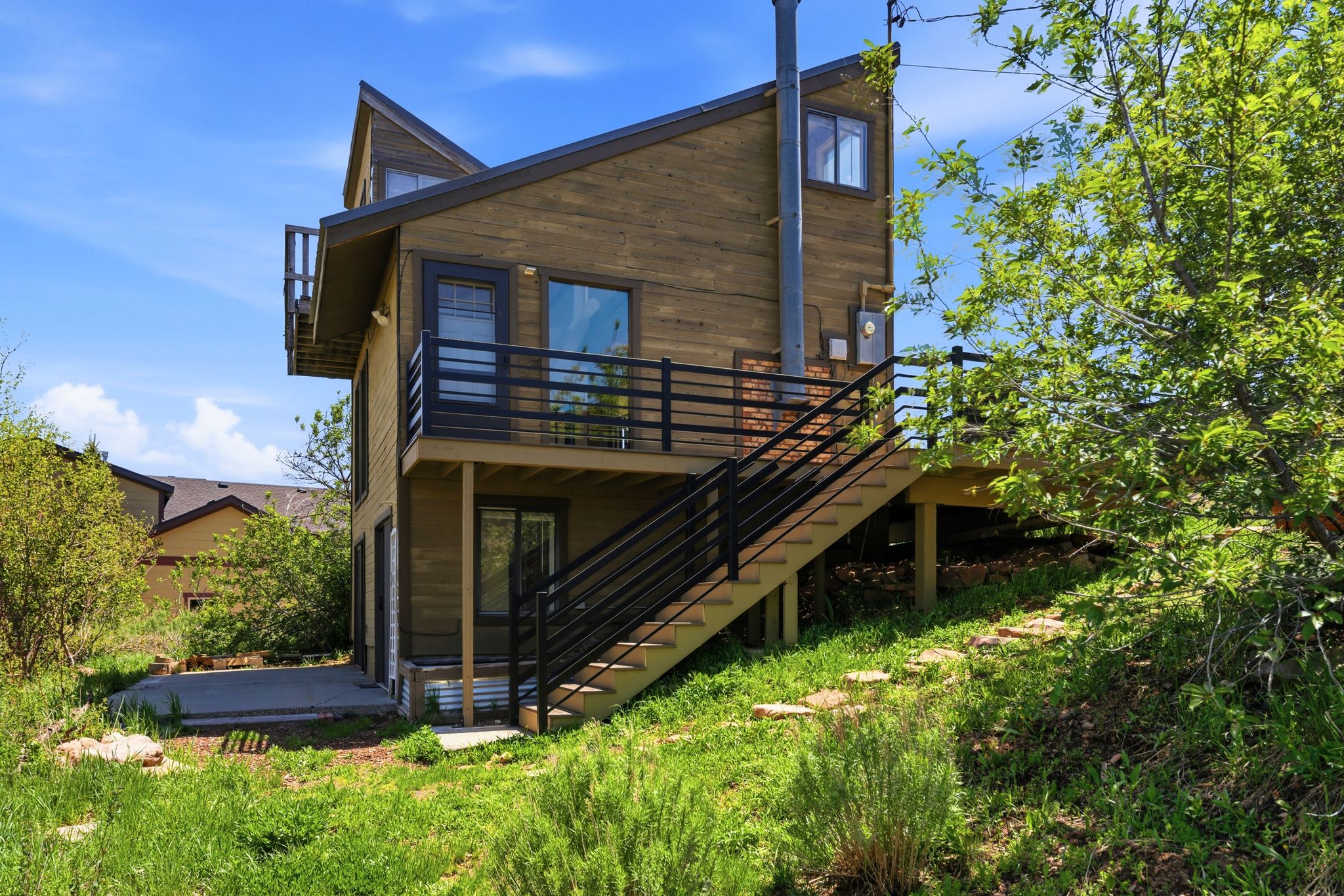 Modern wood-sided residence featuring multiple outdoor decks, a ground-level patio, and exterior stairs with dark metal railings