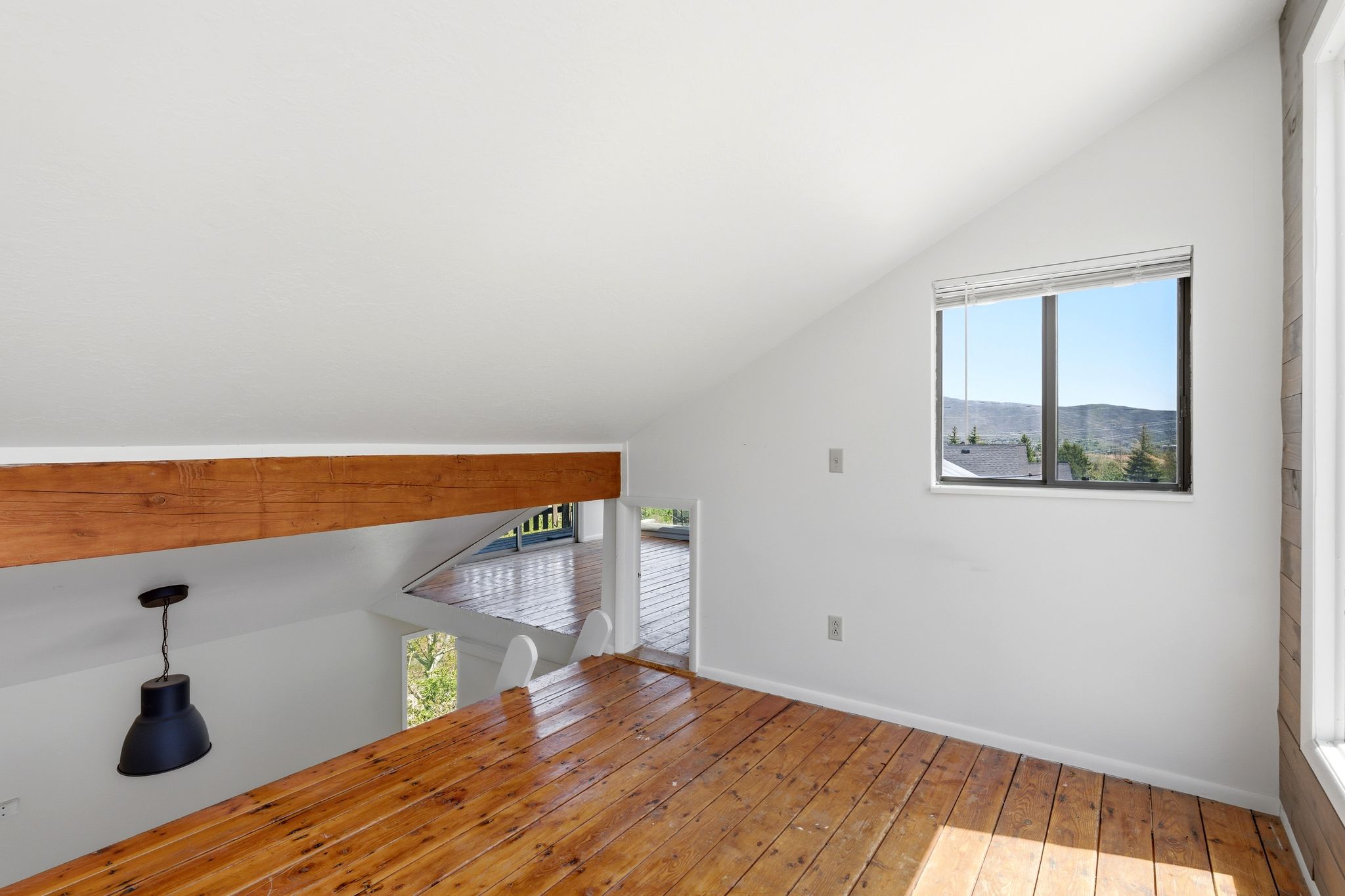 Loft area featuring wood-finish flooring, a prominent wooden beam, and a single window with blinds