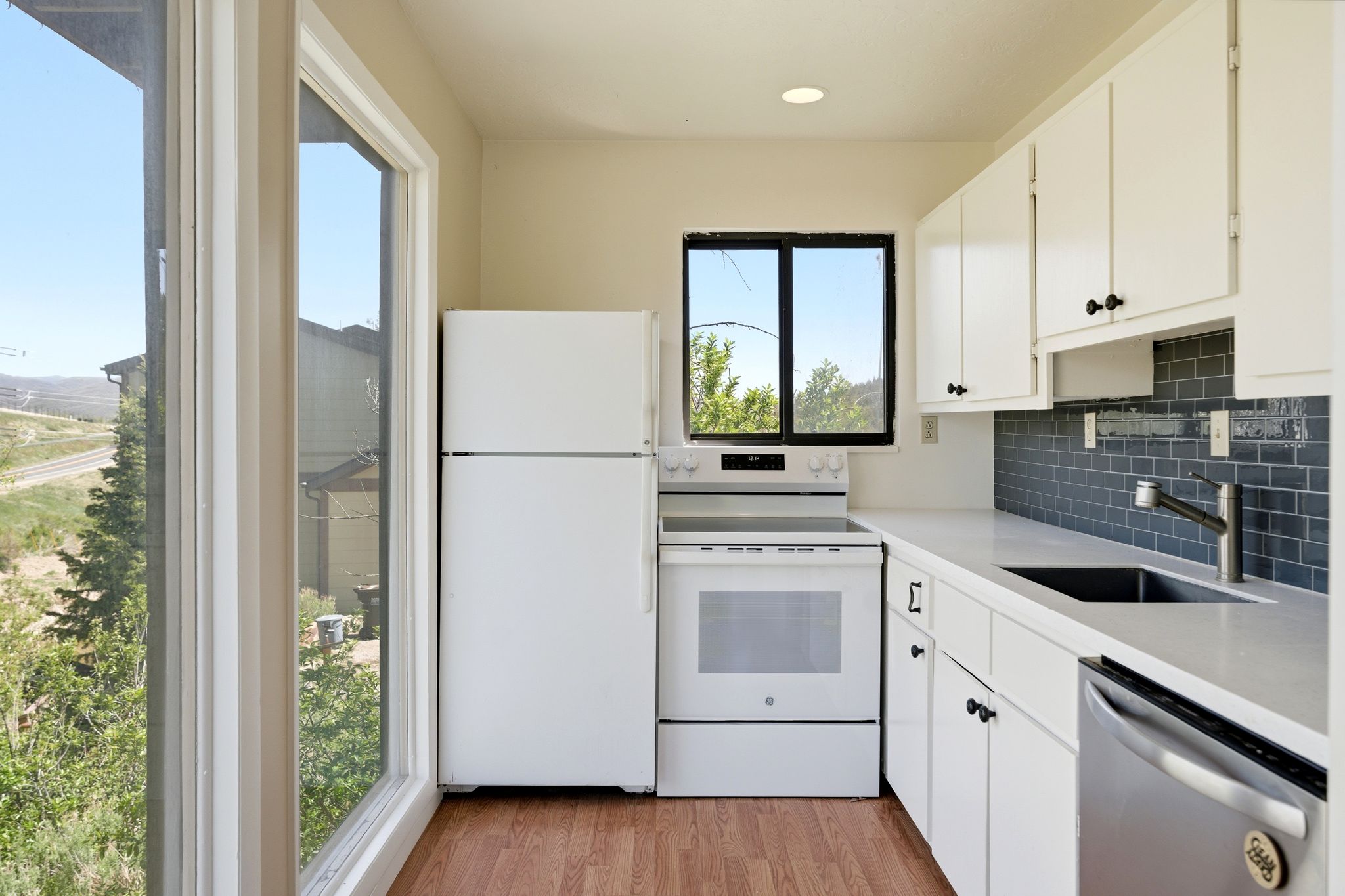 Kitchen featuring white cabinetry, white appliances, a grey subway tile backsplash, white countertops, and wood-finish flooring