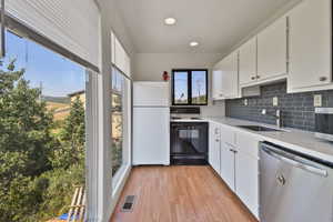 Kitchen with stainless steel dishwasher, electric stove, white cabinets, freestanding refrigerator, and backsplash