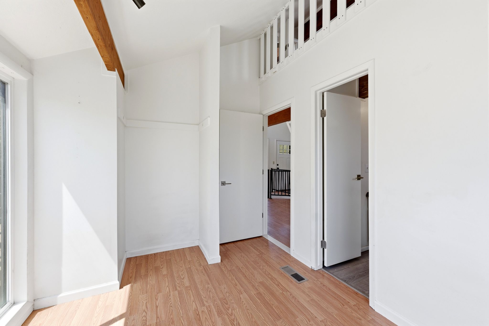 Open concept space featuring wood-finish flooring, white walls, and a light-stained exposed ceiling beam