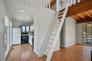 Kitchen with white cabinetry, light countertops, freestanding refrigerator, black range with electric stovetop, and light wood finished floors
