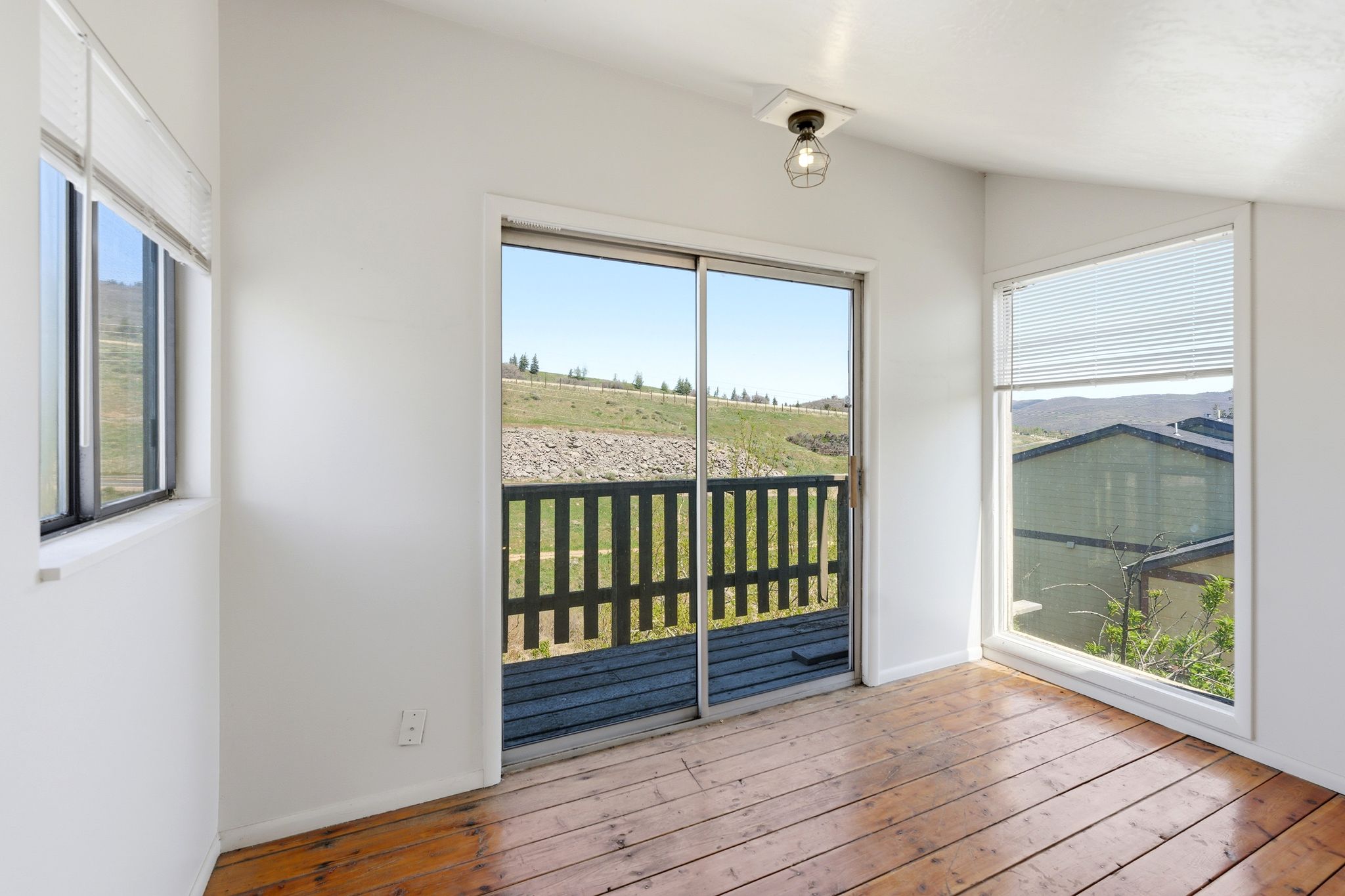 Hardwood flooring with a natural finish, sliding glass door leading to an outdoor deck with a dark railing, and multiple windows providing natural light