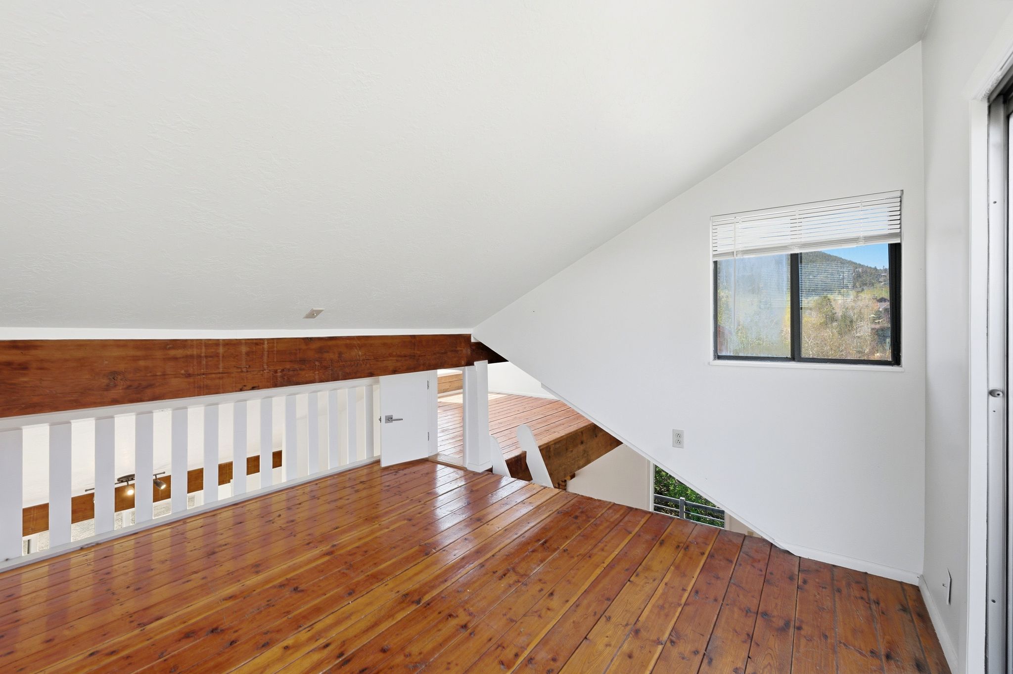 Open loft space featuring wood-finish flooring, white walls, and a sloped ceiling
