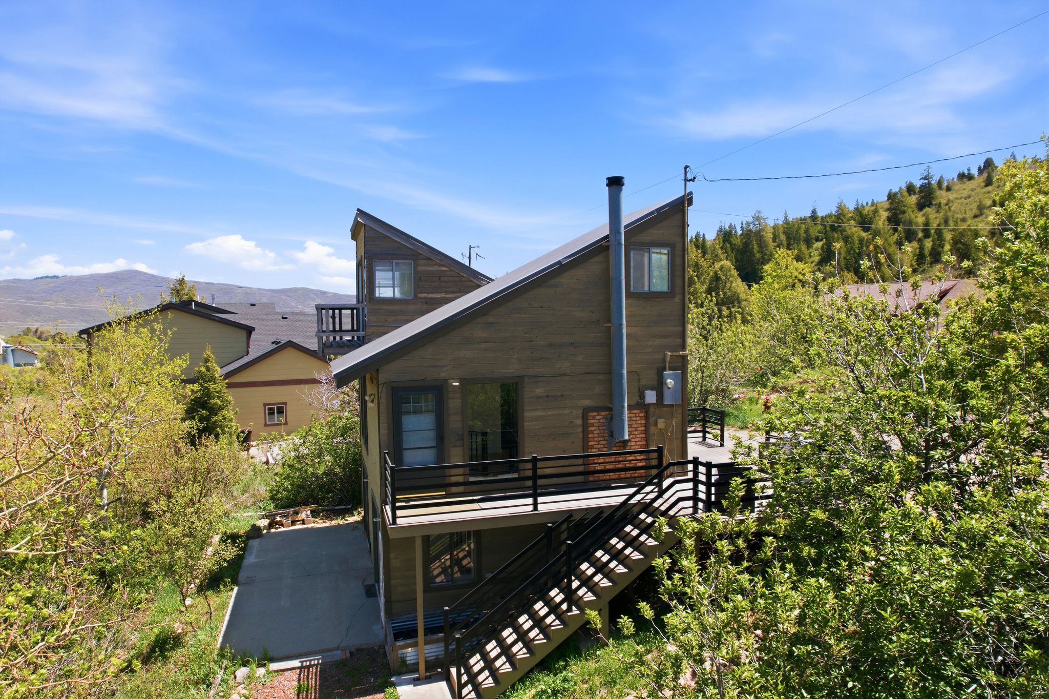Contemporary exterior featuring a distinctive angled roofline, wood-finish siding, multiple balconies with black railings, and a prominent chimney