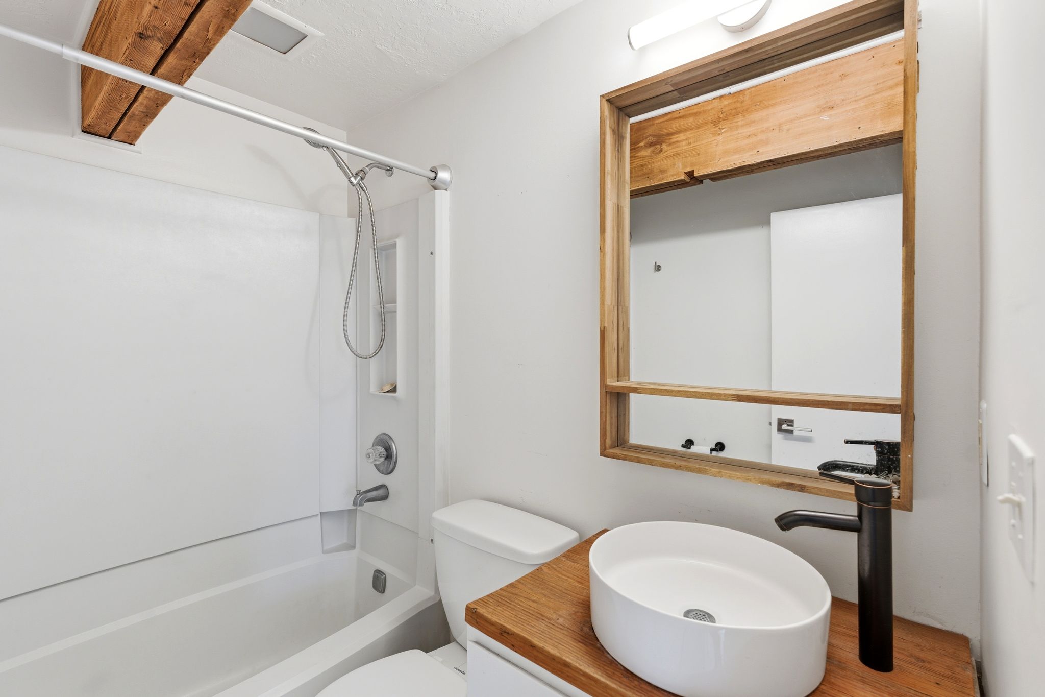 Bathroom featuring a white tub/shower combination, exposed wood beams, and a vessel sink with a matte black faucet