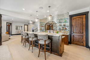 Indoor wet bar featuring hanging light fixtures, backsplash, light stone countertops, wood finish cabinets, and light wood-type flooring