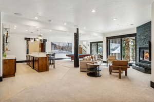 Living area with pool table, a stone fireplace, light carpet, recessed lighting, and wet bar