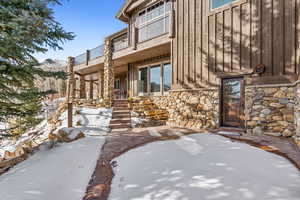 Snow covered property entrance featuring a patio, stone siding, and board and batten siding