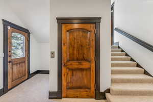 Carpeted entryway featuring stairway and lofted ceiling