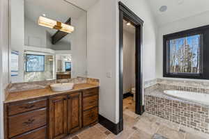 Full bathroom featuring lofted ceiling, vanity, stone tile floors, a garden tub, and recessed lighting