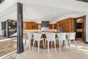 Kitchen with a breakfast bar, wood finish cabinets, a spacious island, backsplash, and light stone counters