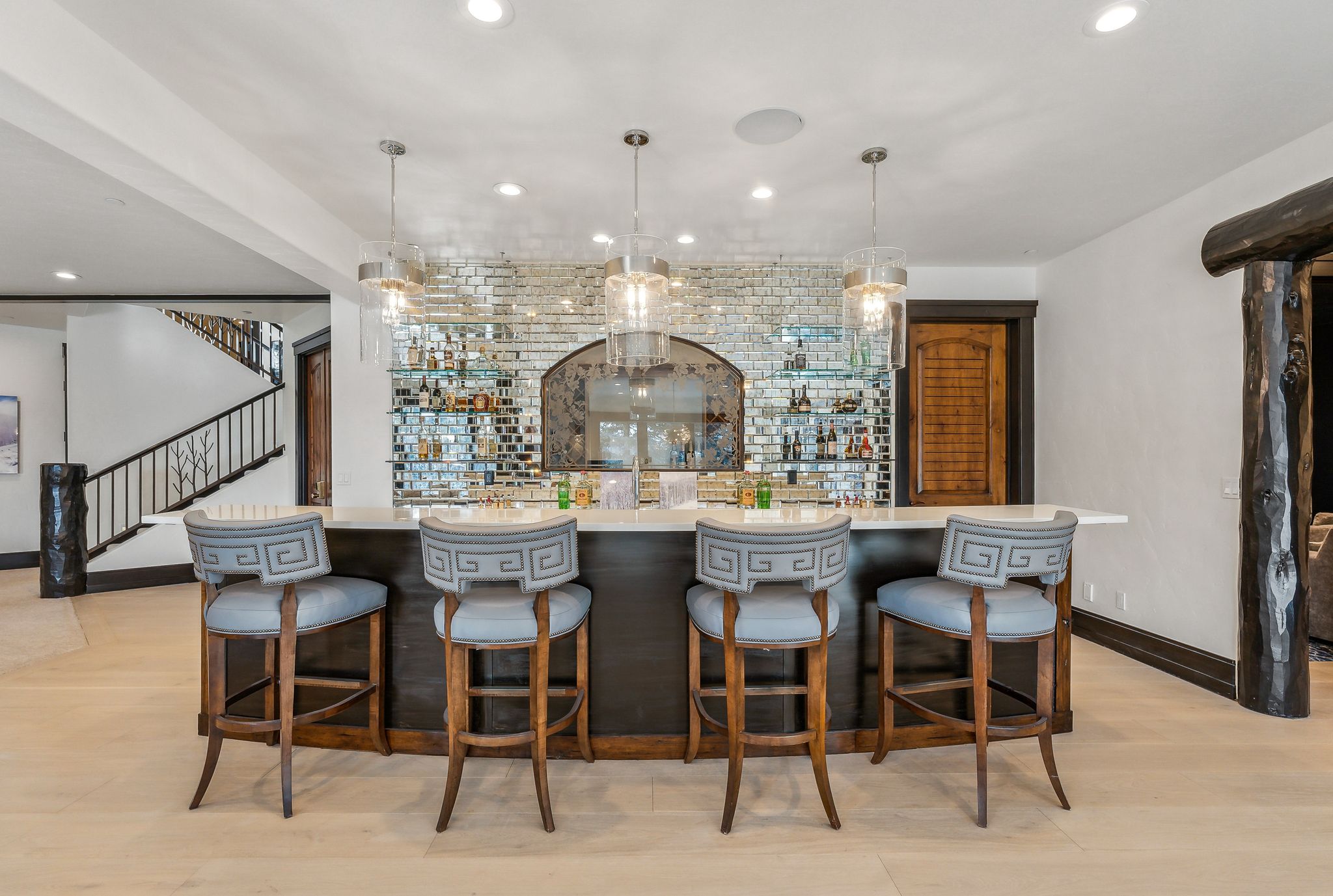 Indoor wet bar featuring light wood finished floors, hanging light fixtures, and light stone countertops