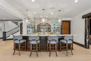 Indoor wet bar featuring light wood finished floors, hanging light fixtures, and light stone countertops