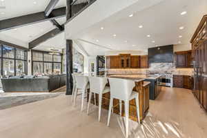 Kitchen with a kitchen bar, glass insert cabinets, open floor plan, light stone countertops, and light wood finished floors