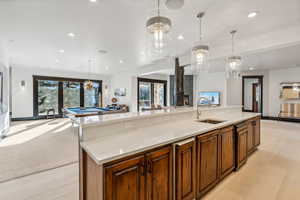 Kitchen featuring open floor plan, wood finish cabinetry, a spacious island, light stone counters, and suspended lighting