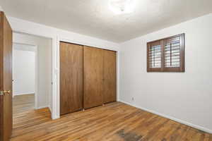 Unfurnished bedroom featuring light wood-style flooring, a textured ceiling, and a closet