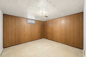 Finished below grade area featuring light flooring, wood walls, and a textured ceiling