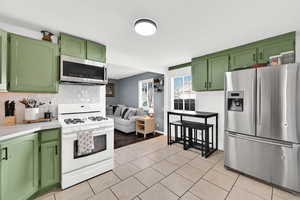 Kitchen featuring green cabinetry, stainless steel appliances, light countertops, backsplash, and light tile patterned floors