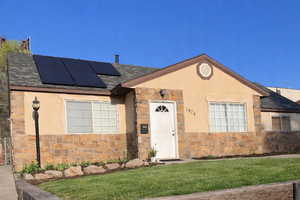 View of front facade featuring stone siding, roof mounted solar panels, and a shingled roof